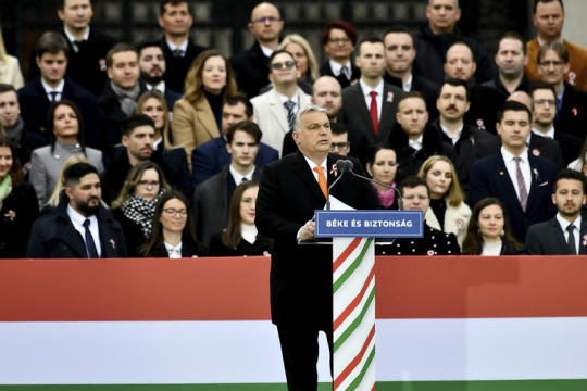 Orbán Viktor beszédet mond egy tömeg előtt, Béke és Biztonság feliratú pulpitusnál.