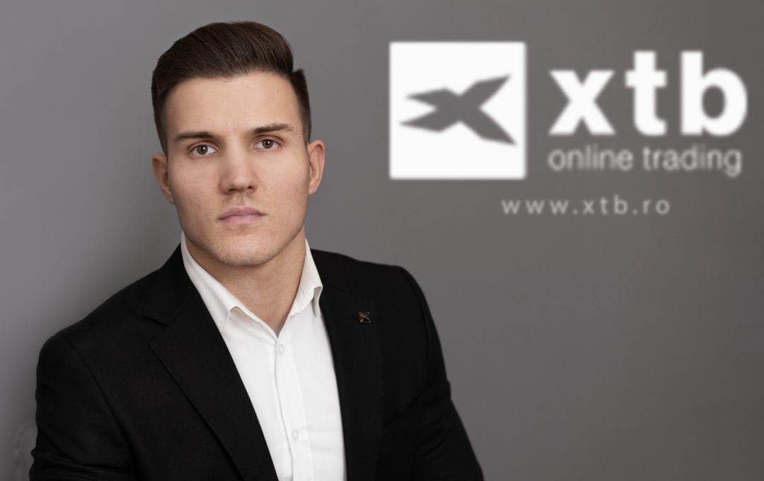 Férfi öltönyben, az XTB online trading logója a háttérben.