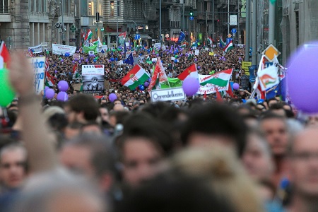 Nagy tömeg tüntet az utcán, magyar zászlók láthatók.